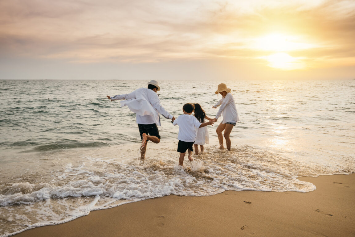 Family of four dressed in white dance on a beach at sunset
